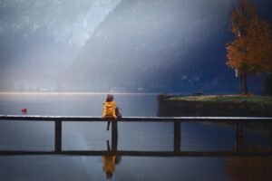 A person crossing a bridge over a mountain lake, representing the path clients take to find a therapist
